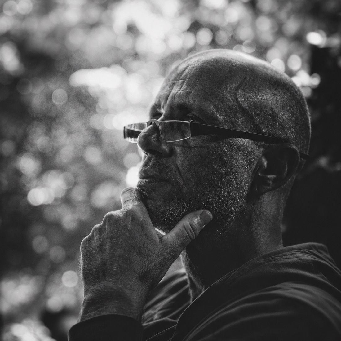 Oliver Wattenberg im Halbprofil, mit Brille und der Hand am Kinn, nachdenklicher Blick, Schwarz-Weiß-Aufnahme im Gegenlicht.