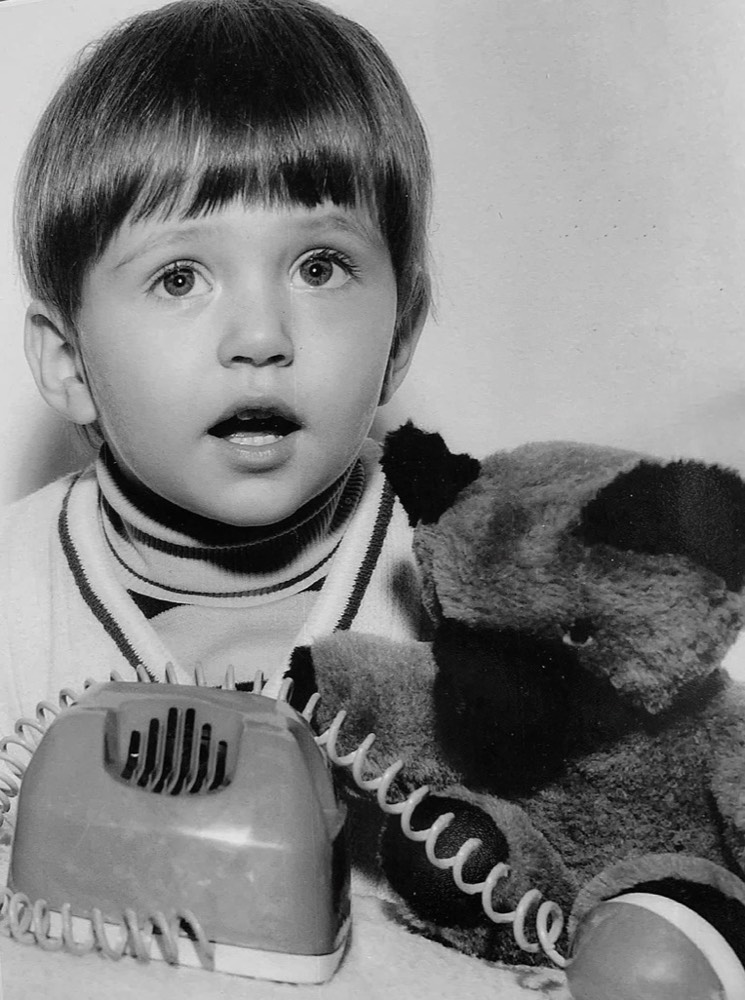 Oliver Wattenberg als kleines Kind, mit einem Spielzeugtelefon und einem Plüschtier, historische Schwarz-Weiß-Aufnahme.