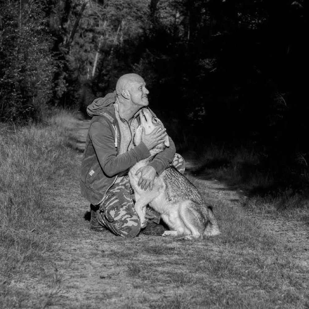 Oliver Wattenberg kniet auf einem Waldweg und hält seinen Wolfshund im Arm, Gegenlicht, Schwarz-Weiß.